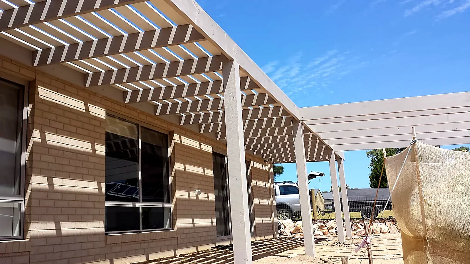 Timber pergola shade structure under construction beside a brick house