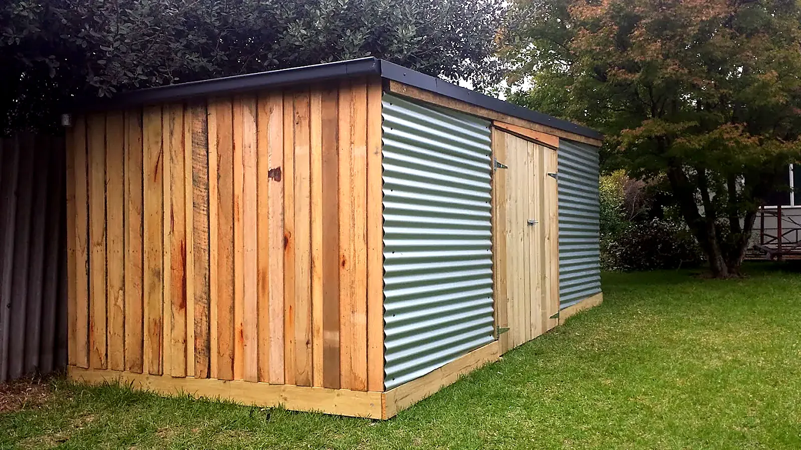 Timber-clad outbuilding with corrugated iron walls and double doors